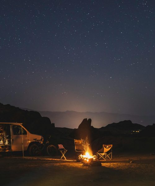 A serene night camping scene with a van, tents, and campfire beneath a starry sky.