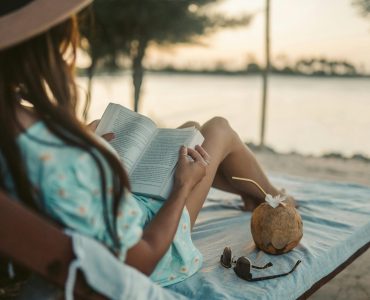 Woman enjoys a peaceful sunset reading session on Zanzibar beach with a coconut drink nearby.