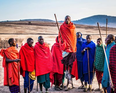A group of Maasai men in vibrant traditional attire performing a cultural jumping dance outdoors.