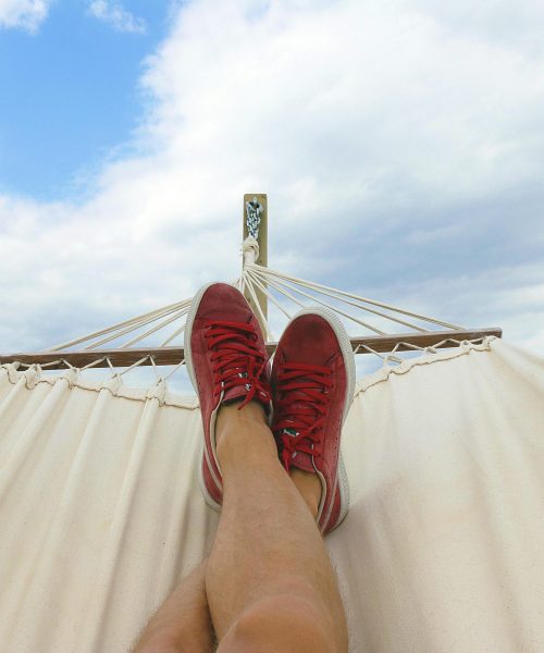 Feet resting on a hammock with red sneakers, epitomizing summer relaxation and leisure outdoors.